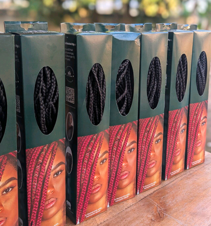 [color:Black] Several boxes of black braided hair extensions arranged in a row on a wooden surface, with oval cutouts showing the black braids inside and printed model photos on the front.